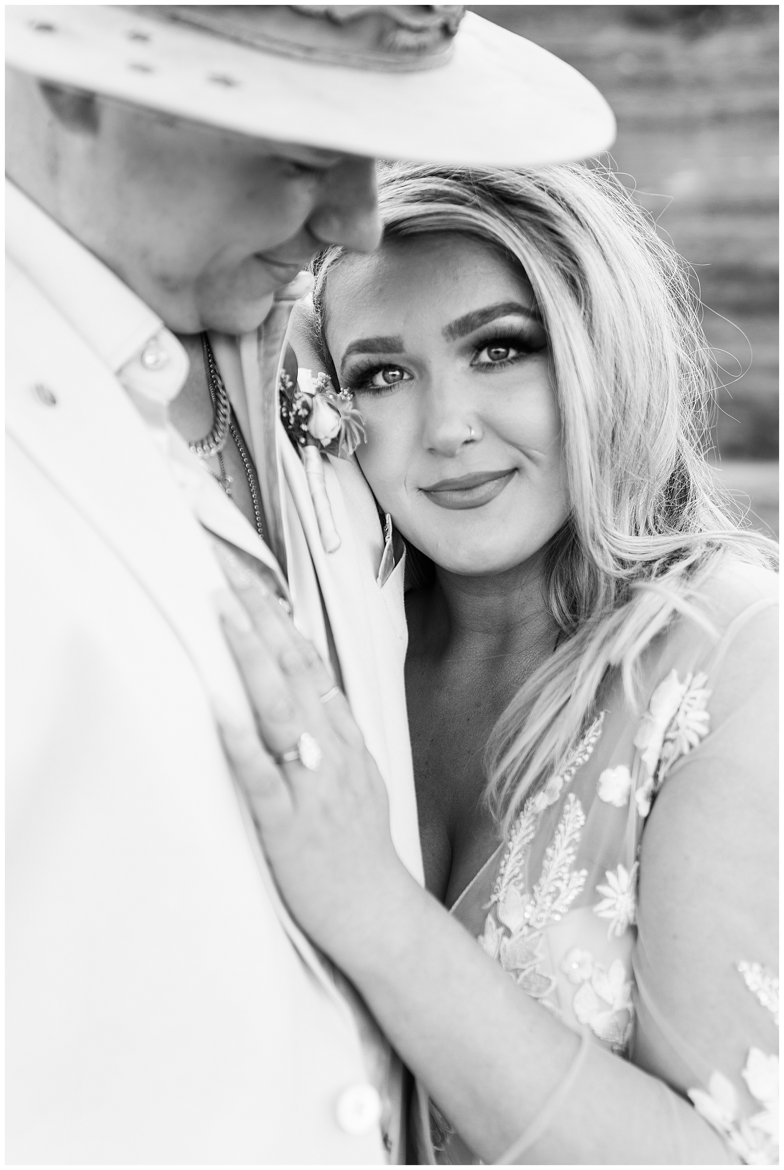 Black and white photo of groom looking down at his bride while she stares into the camera