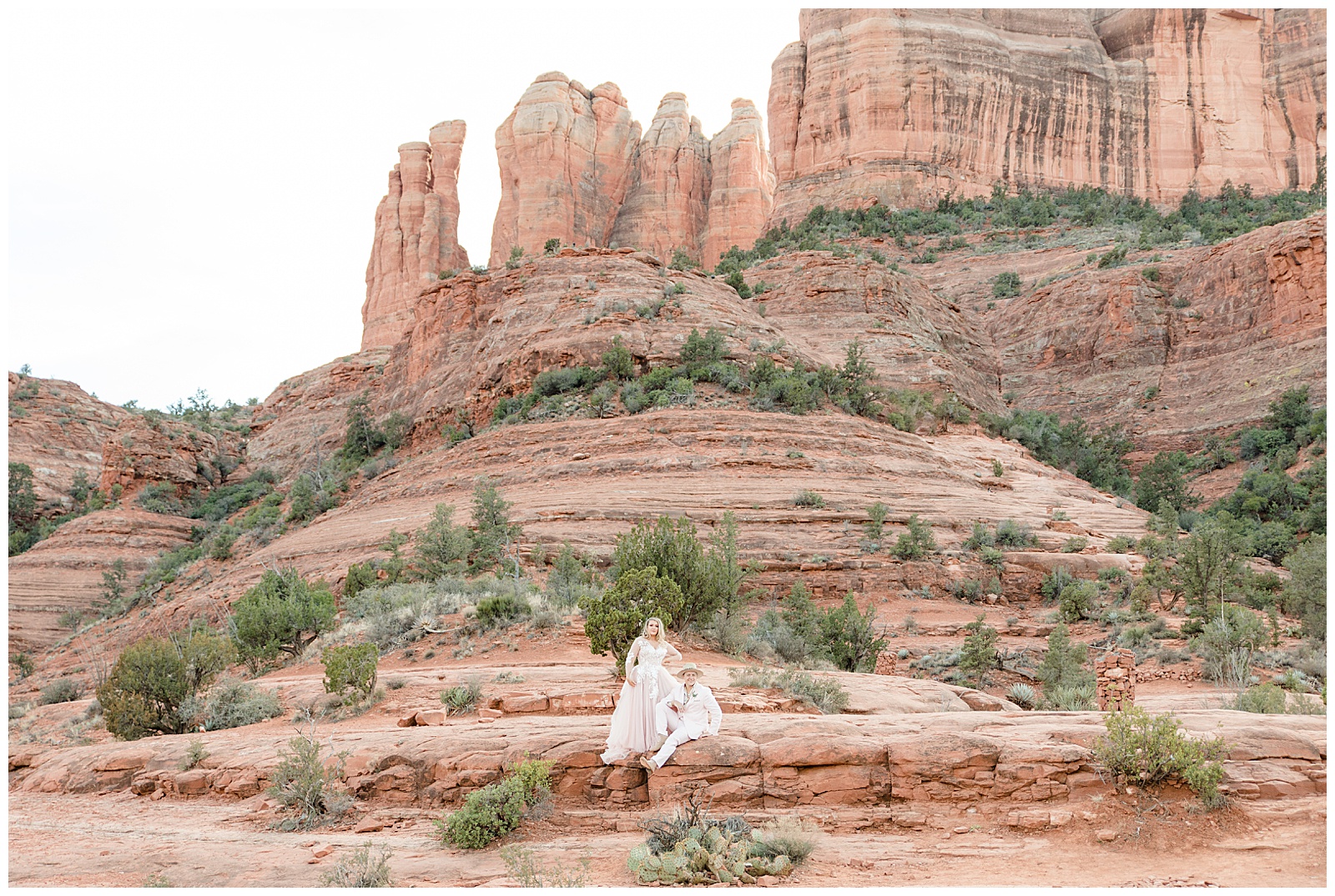 Groom sits on the rocks while bride admires the view of Sedona